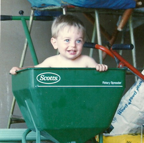 Small boy sitting inside Scotts fertilizer spreader